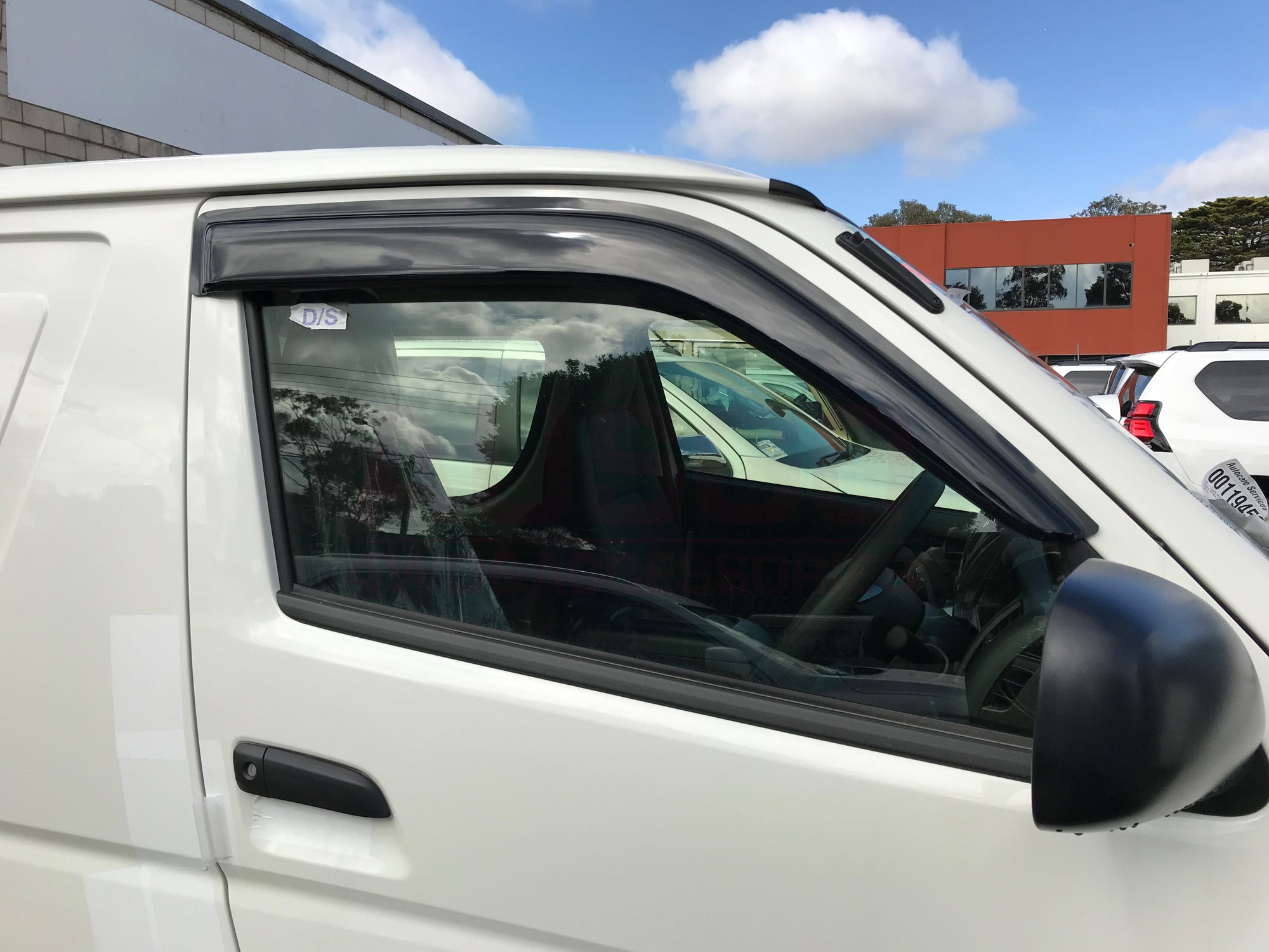 Side view of the driver's seat of a white Toyota HiAce van with weather shields attached to the window.
