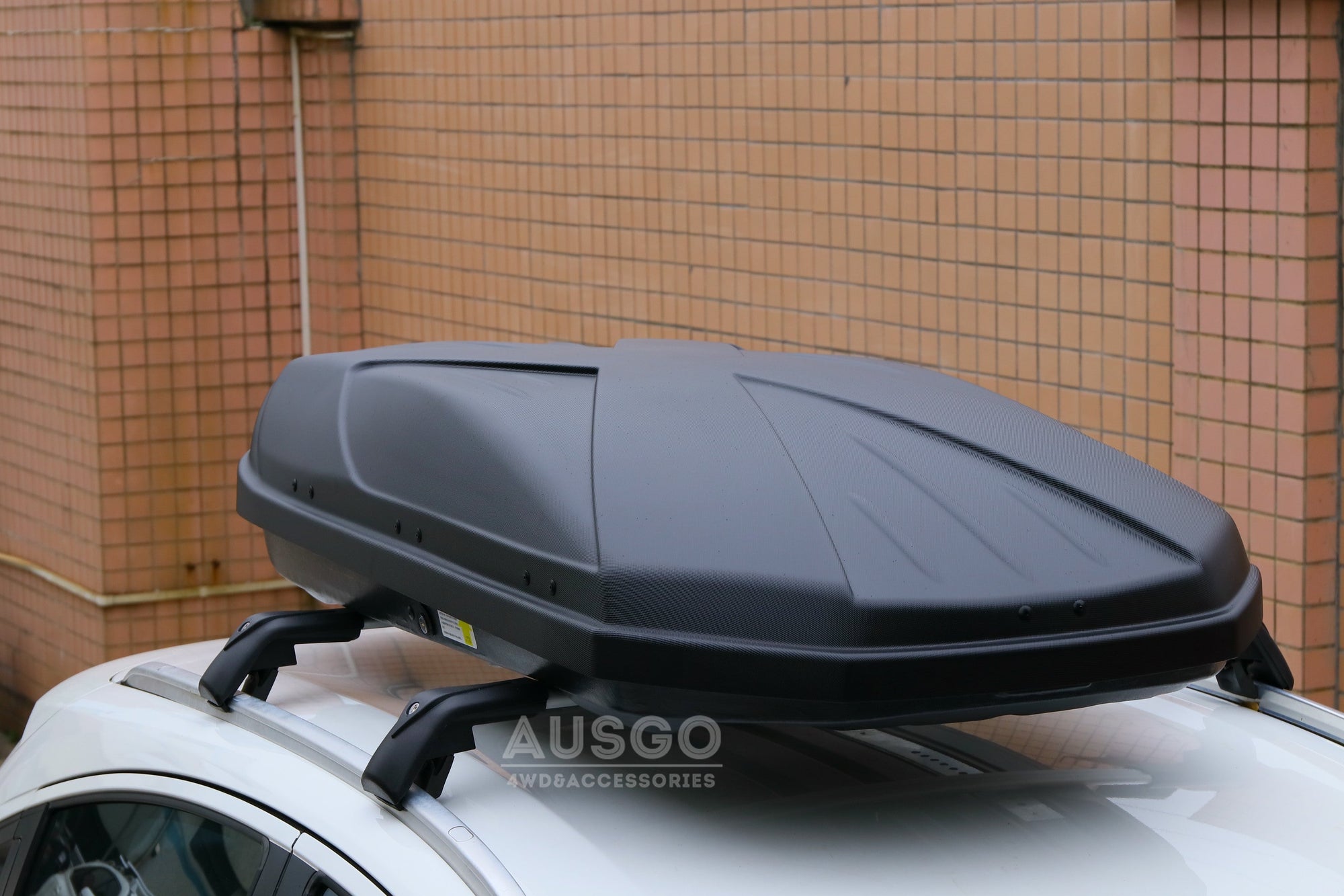 A sleek black rooftop cargo box mounted on cross bars on a white car.