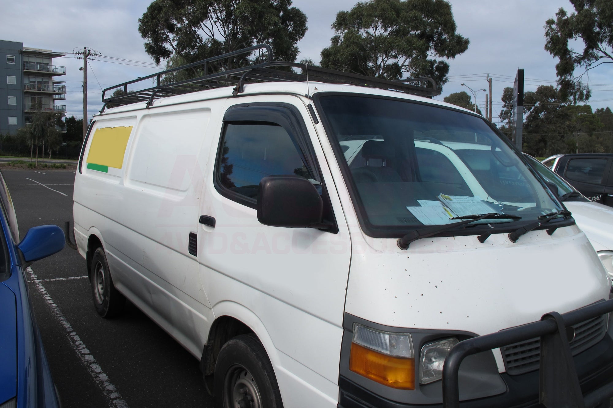 A white Toyota HiAce parked in an outdoor carpark.
