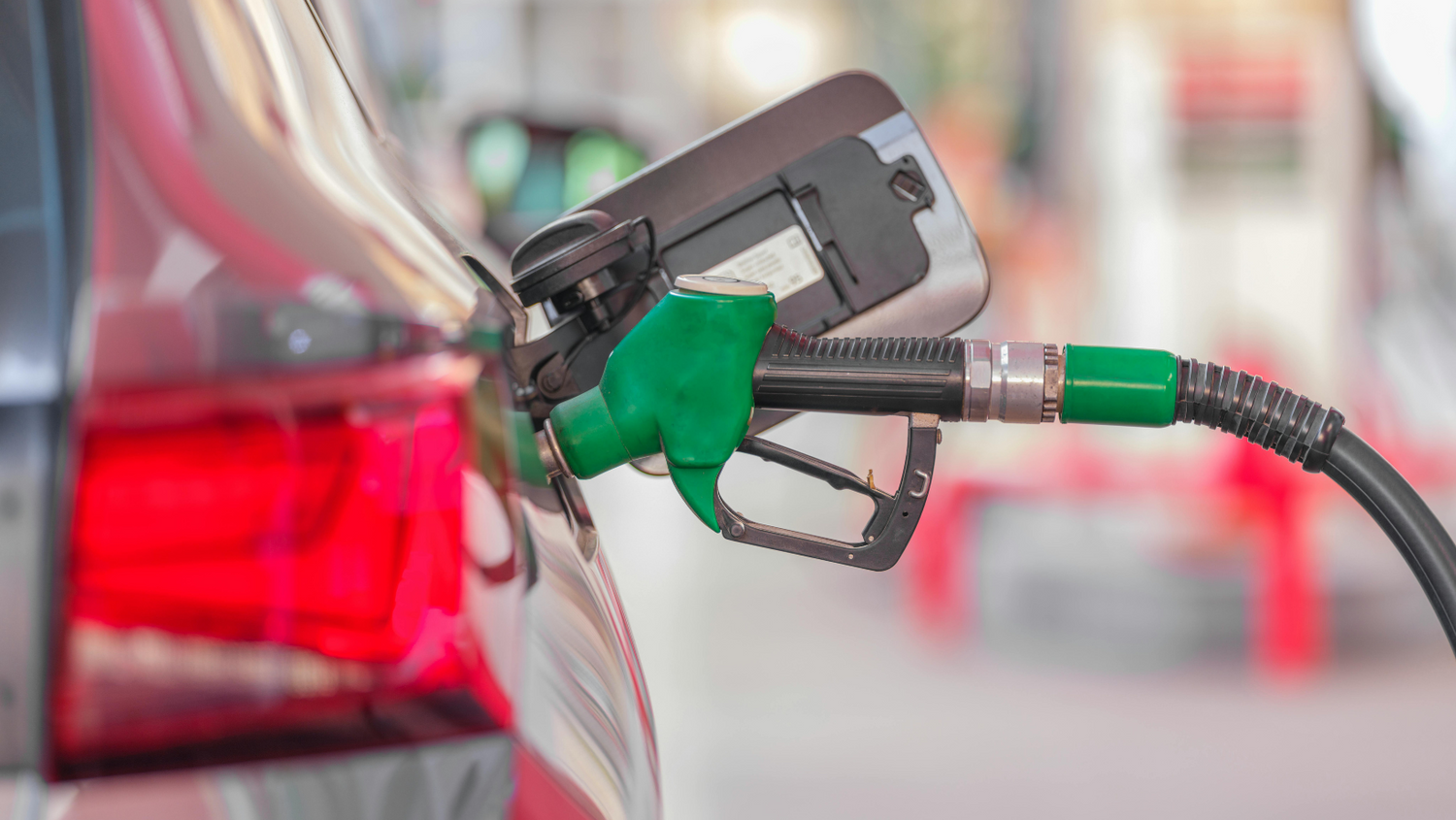 Close-up of a green fuel nozzle inserted into a car's fuel tank at a petrol station, highlighting fuel refilling