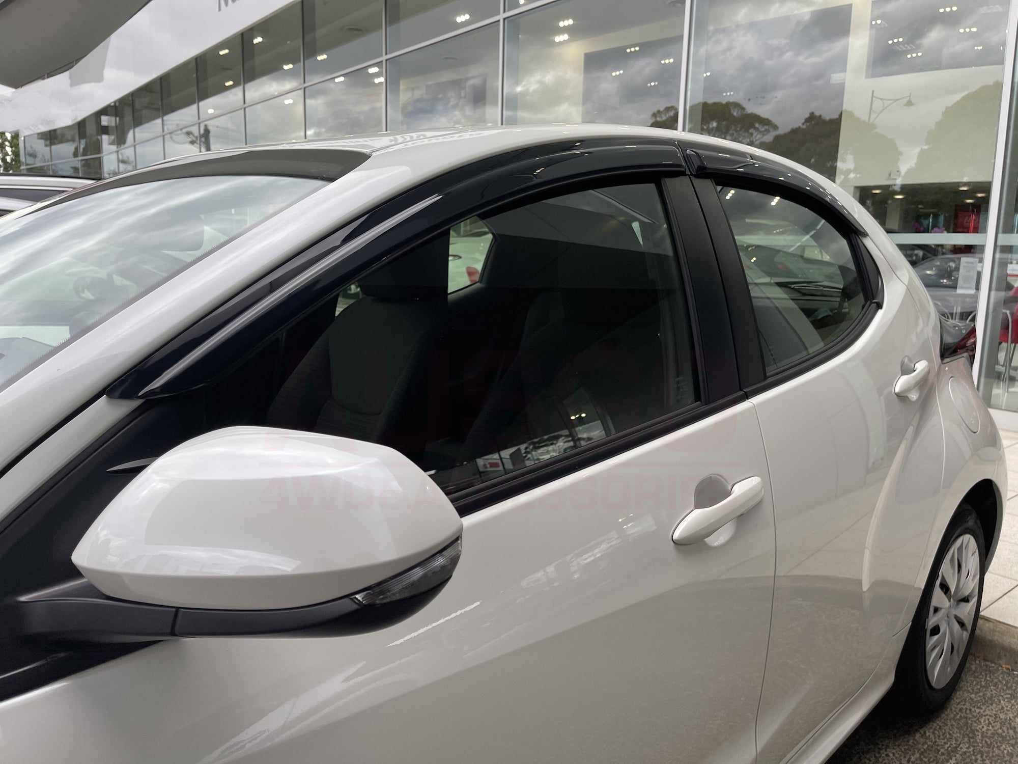 Side view of a white Toyota Yaris with black weather shields attached to the windows.
