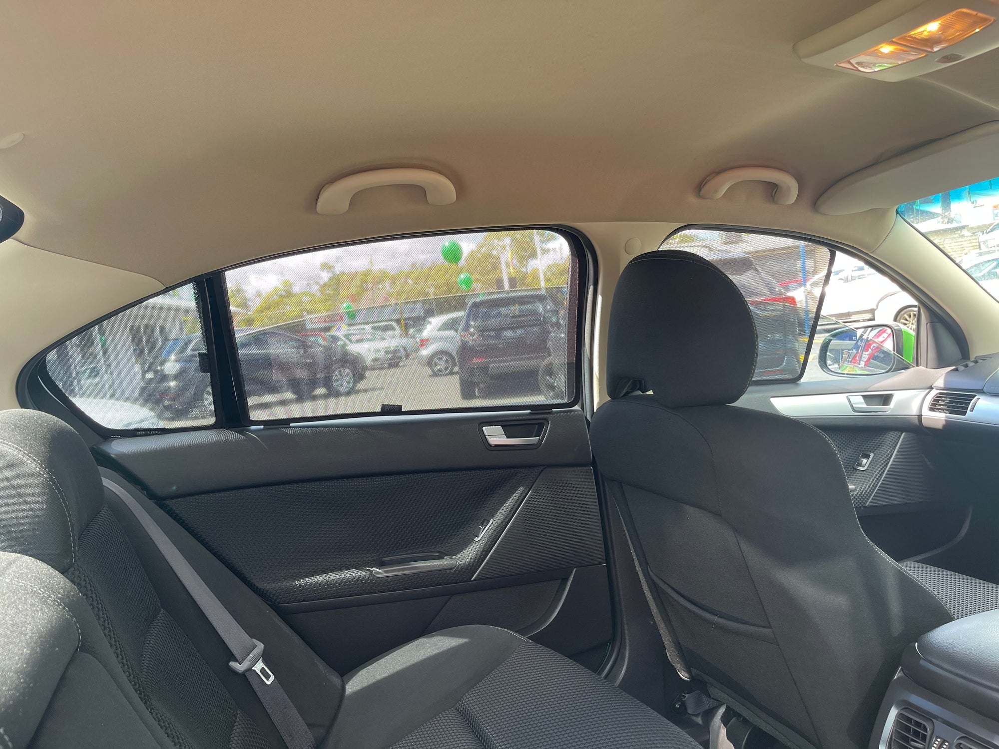 View from the backseat of a car, showing two black front seats with sun shades attached to the window.